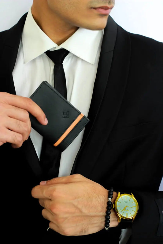 Man in a suit holding a black wallet with an orange accent, wearing a gold watch.