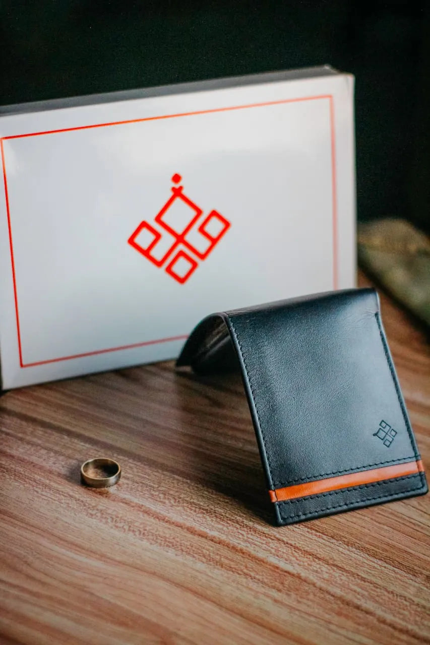 Black leather wallet with orange accent on a wooden surface, with a branded box in the background.